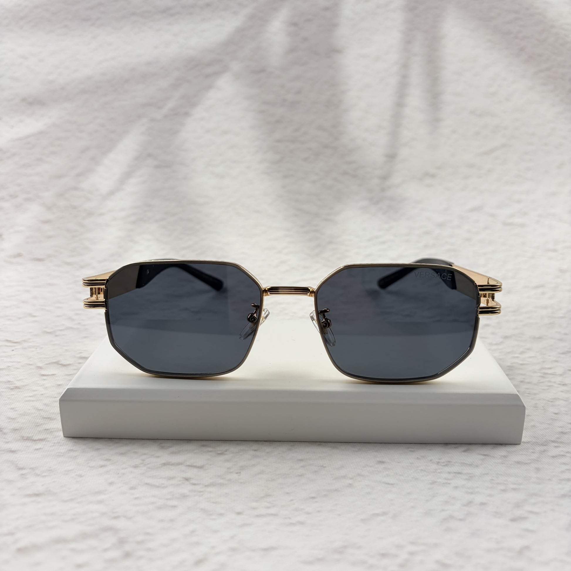 Gold tone metal frame geometric sunglasses with dark lenses on a white display block.
