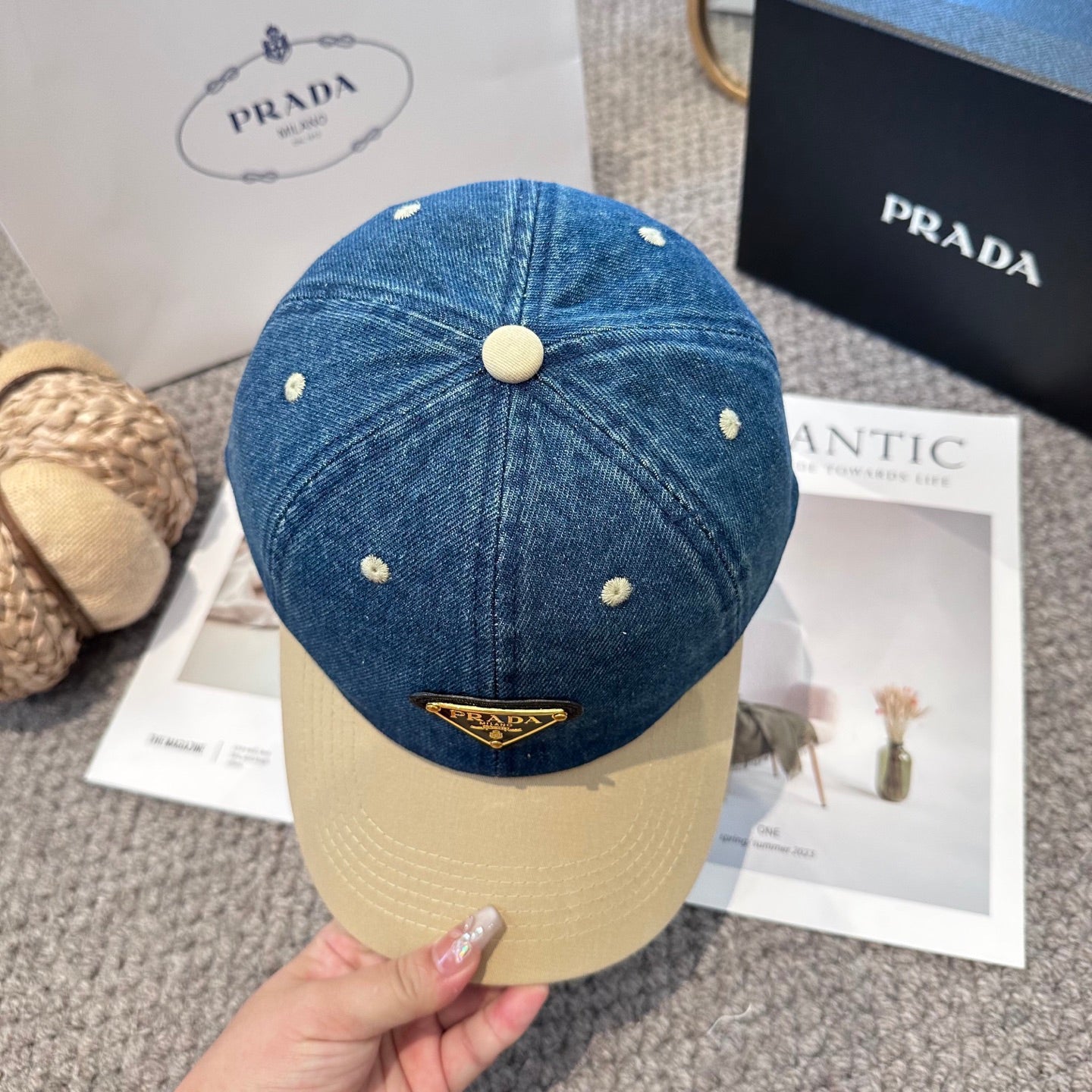 A two-tone baseball cap with a blue denim crown, beige brim, and a triangular metal logo badge.