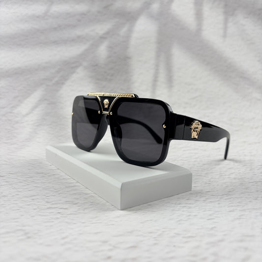 Oversized black flat-top sunglasses with a gold metal bridge and gold emblems on the temples.