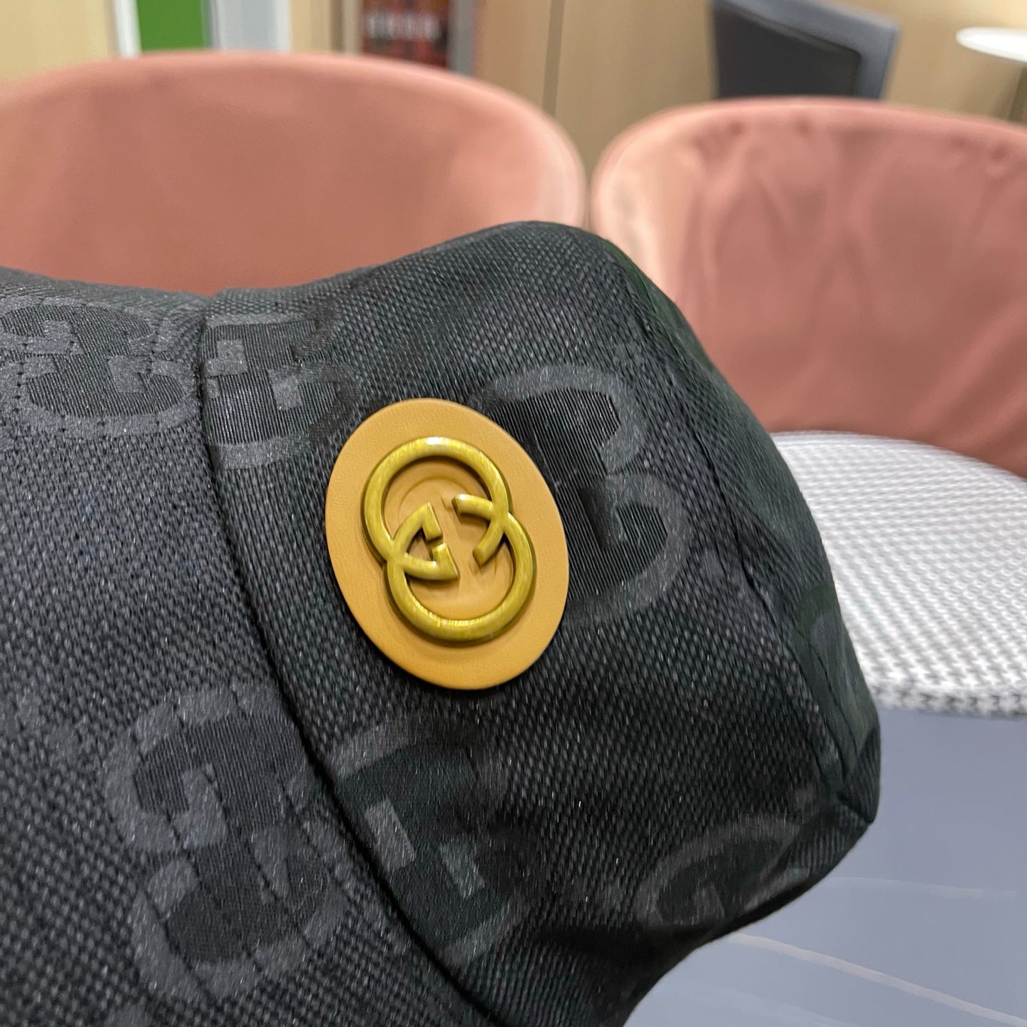 A black textured bucket hat with a circular gold emblem, featuring a monogrammed fabric design.