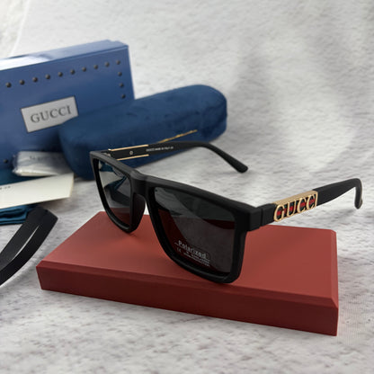Matte black polarized sunglasses with gold logo detailing on temple arms, sitting on a red display b