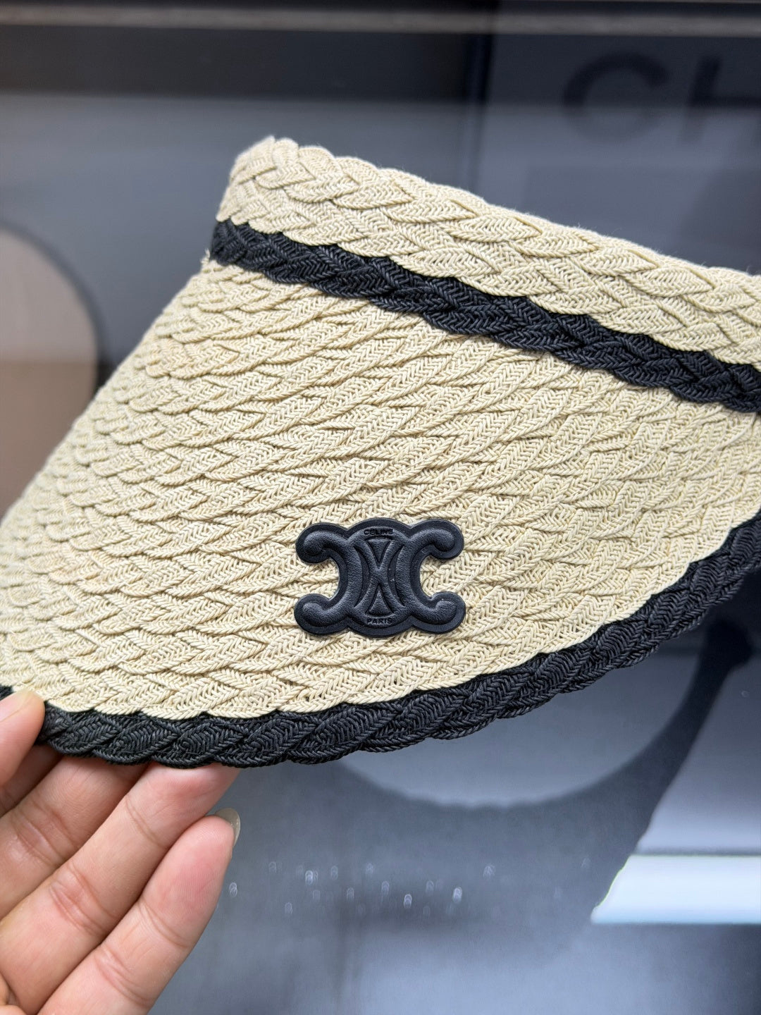 Woven straw sun visor with black contrast trim and decorative logo detail for summer protection.