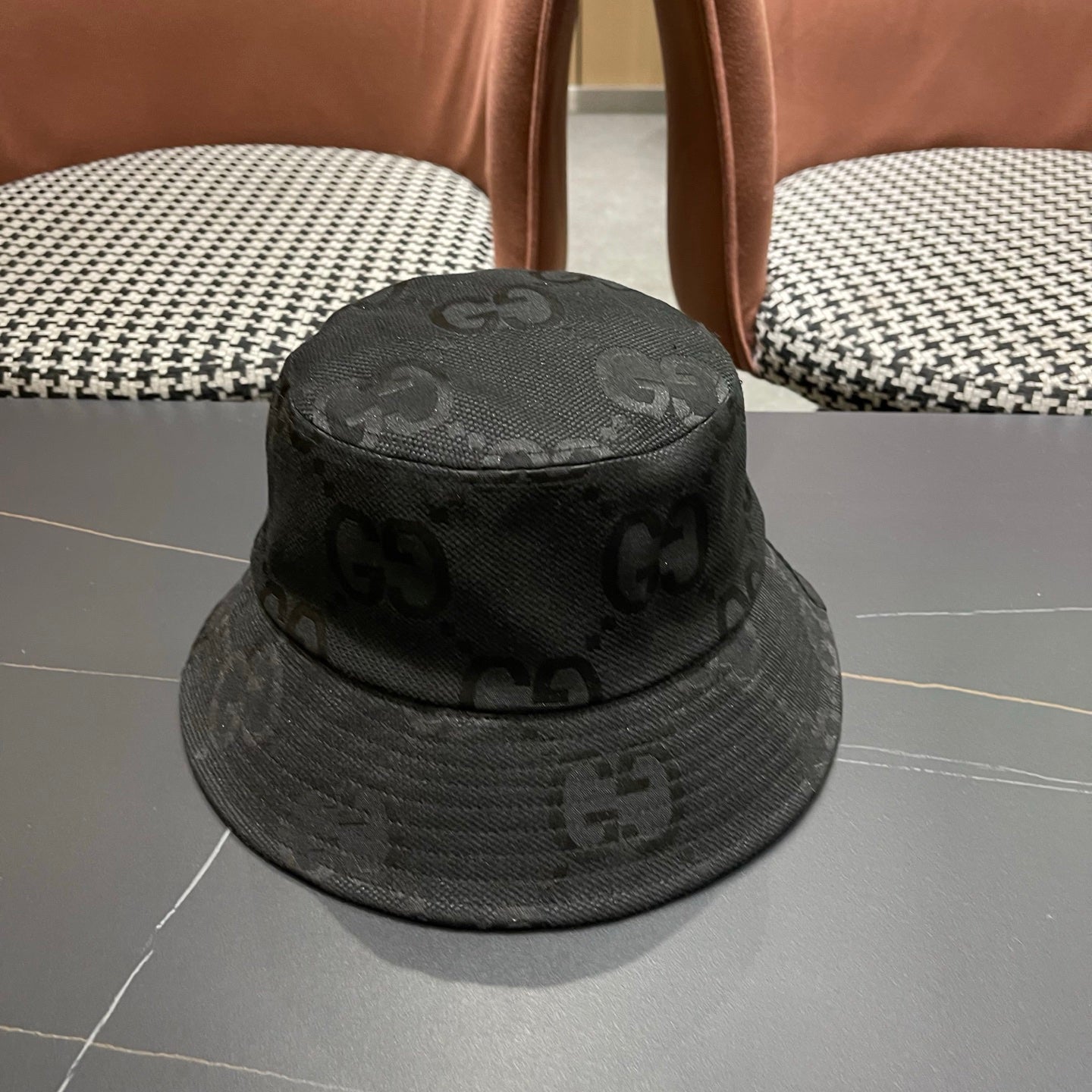 A black textured bucket hat with a circular gold emblem, featuring a monogrammed fabric design.