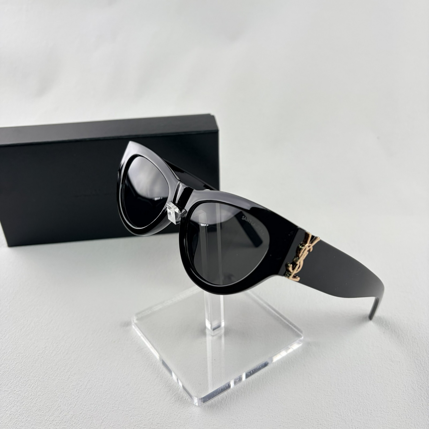 A pair of black cat-eye sunglasses with gold-tone hardware on the temples, displayed on a stand.