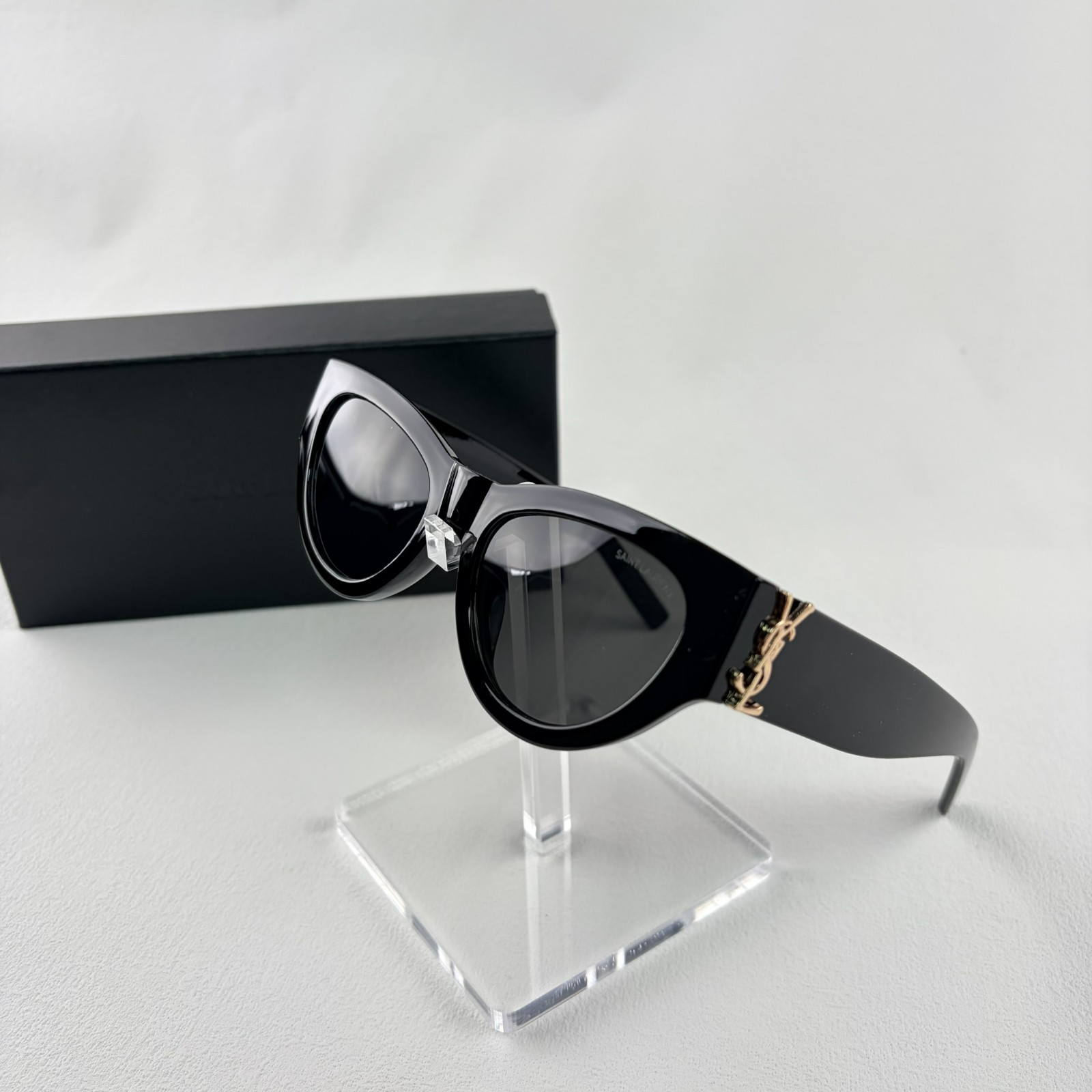 A pair of black cat-eye sunglasses with gold-tone hardware on the temples, displayed on a stand.