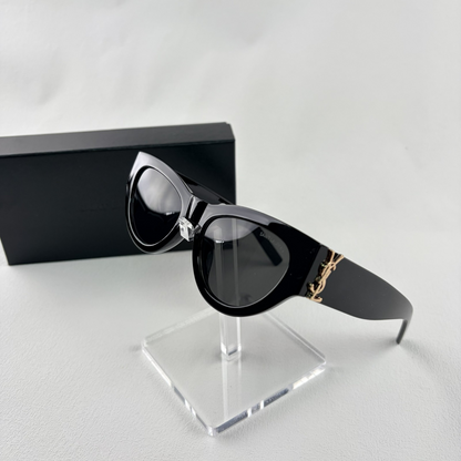 A pair of black cat-eye sunglasses with gold-tone hardware on the temples, displayed on a stand.