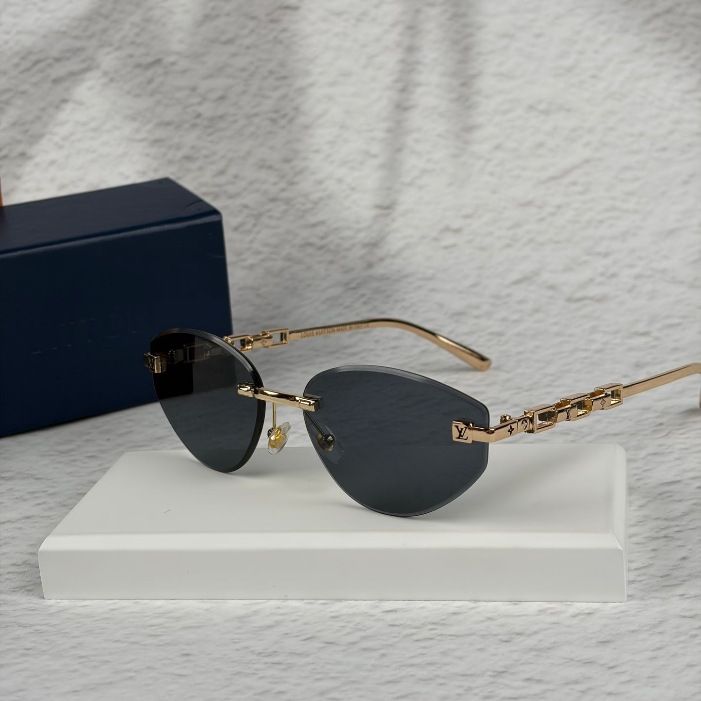 Rimless sunglasses with gold metal arms and dark gradient lenses resting on a white display block.