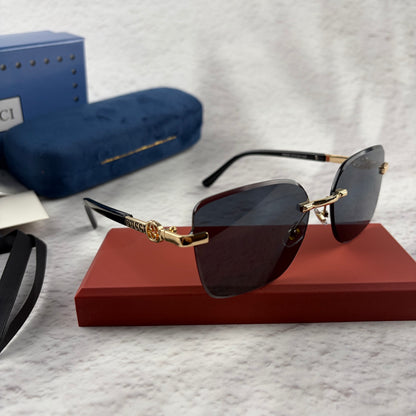 Rimless rectangular sunglasses with gold-tone metal arms and dark lenses on a red display stand.