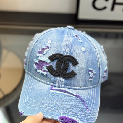 Distressed blue denim baseball cap with frayed detailing and a central stitched logo emblem.