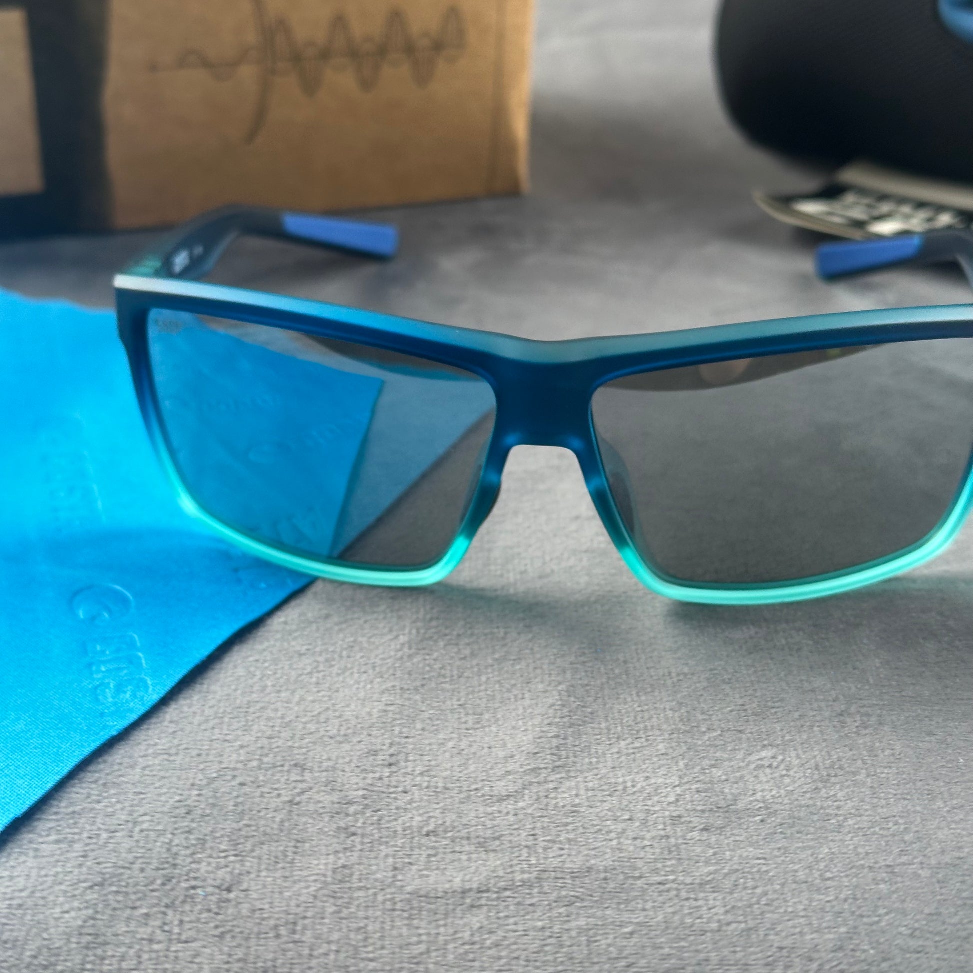 Blue and teal gradient frame sport sunglasses with polarized lenses resting on a blue cloth.
