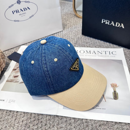 A two-tone baseball cap with a blue denim crown, beige brim, and a triangular metal logo badge.