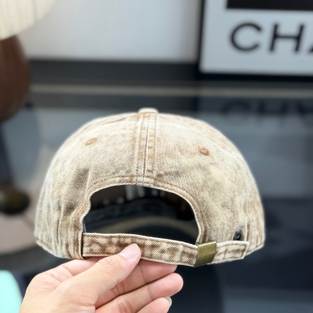 Vintage style distressed light brown denim baseball cap with embroidered letter patch on front.