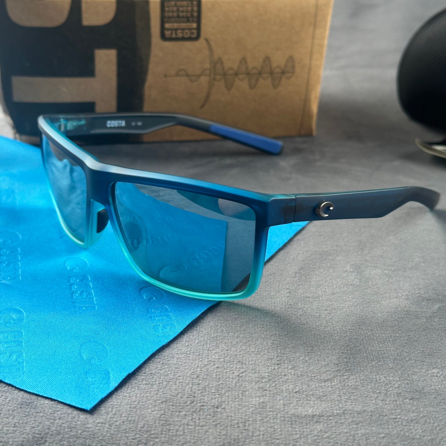 Blue and teal gradient frame sport sunglasses with polarized lenses resting on a blue cloth.