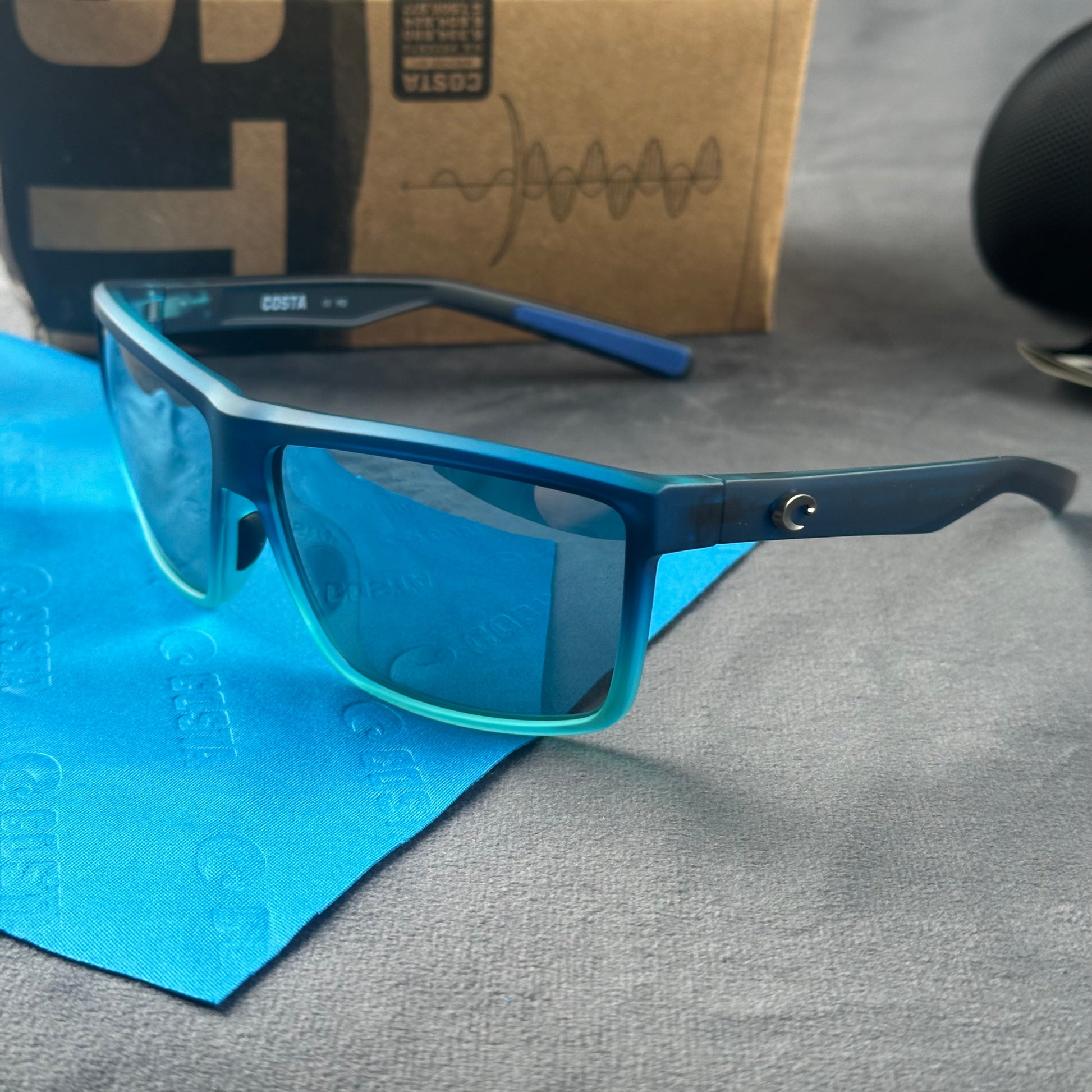 Blue and teal gradient frame sport sunglasses with polarized lenses resting on a blue cloth.
