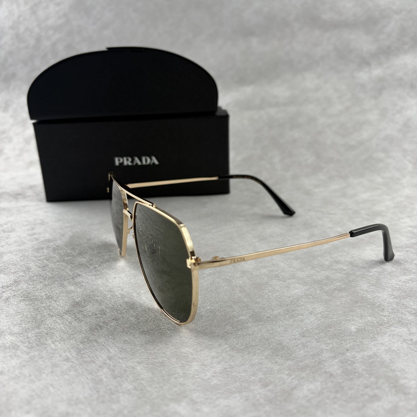 Classic gold-tone metal aviator sunglasses with tinted lenses, resting next to a protective case.