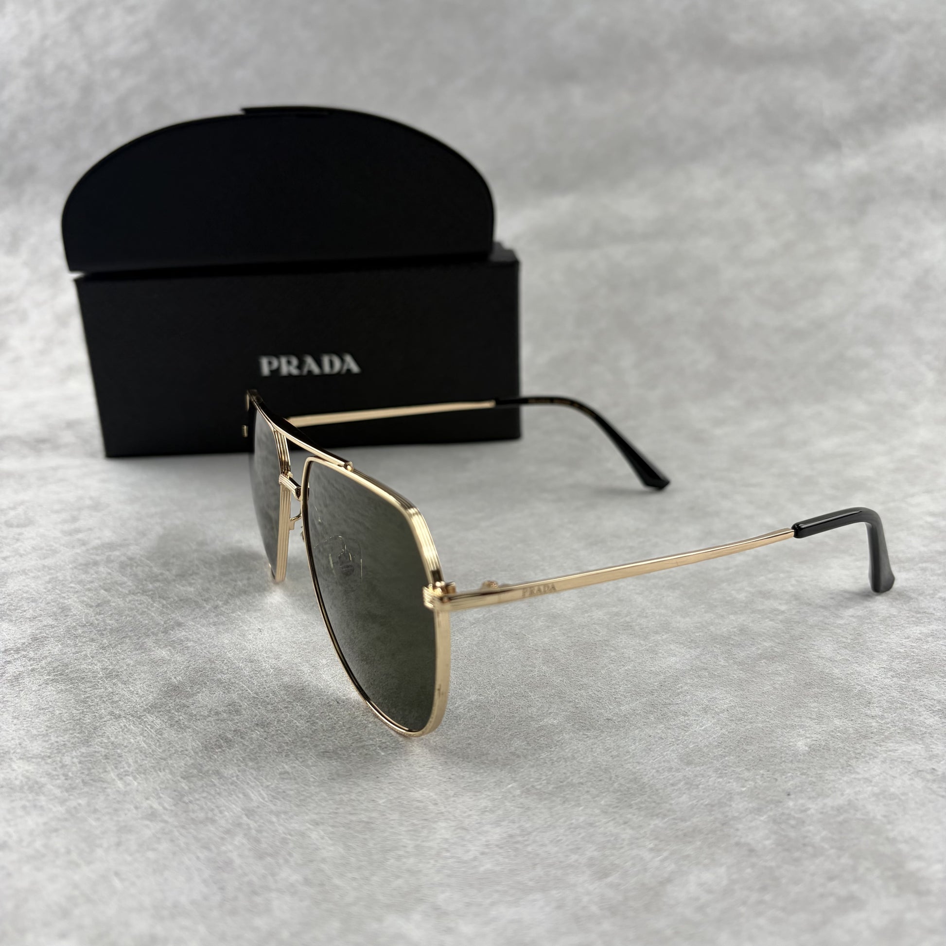 Classic gold-tone metal aviator sunglasses with tinted lenses, resting next to a protective case.