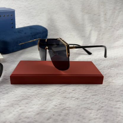 Oversized shield sunglasses with a gold metal frame and dark black lenses on a red display stand.