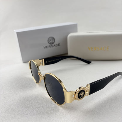 Oval gold metal frame sunglasses with black temples and dark tinted lenses, shown with a storage cas