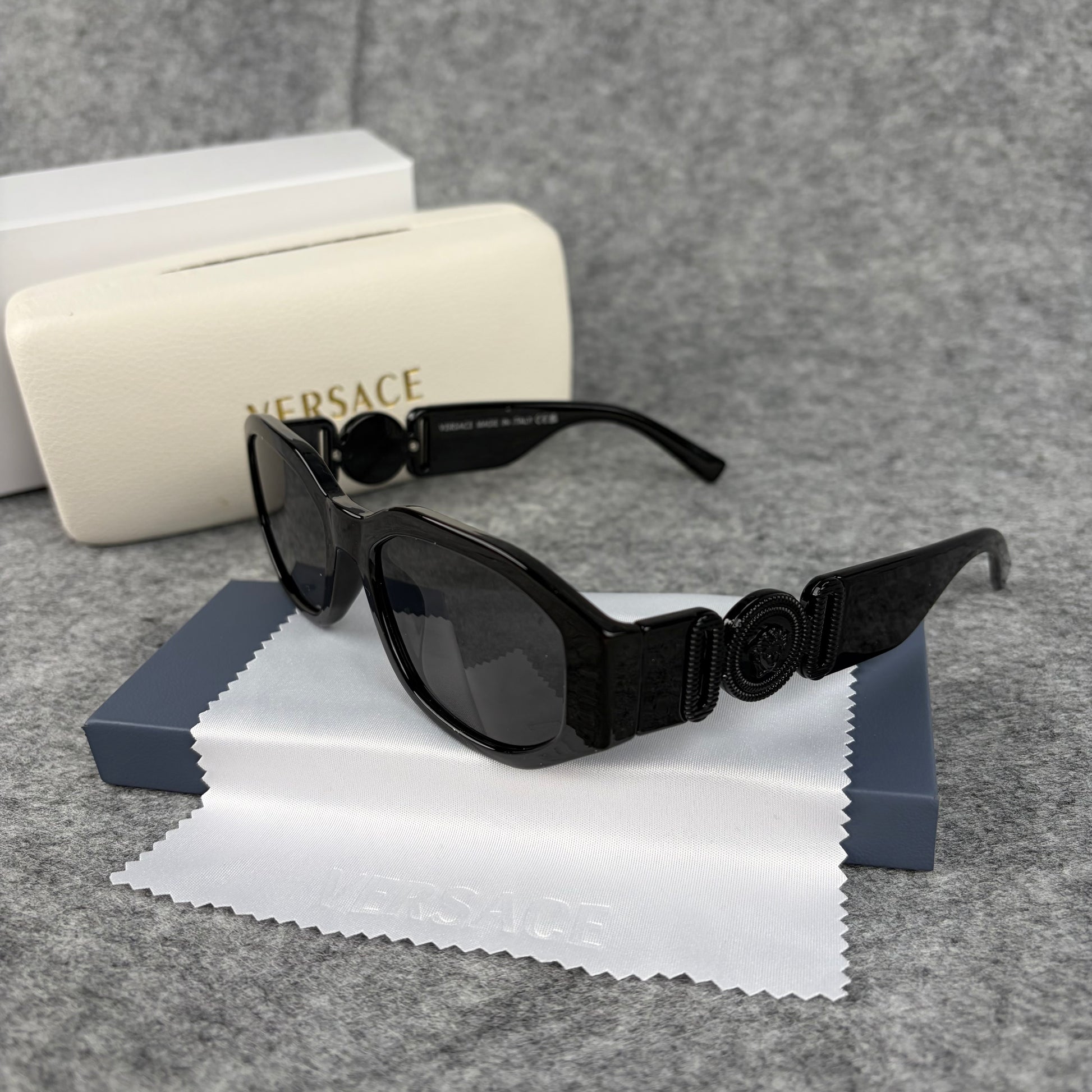 A pair of sleek black oval sunglasses resting on a cleaning cloth next to a white protective case.
