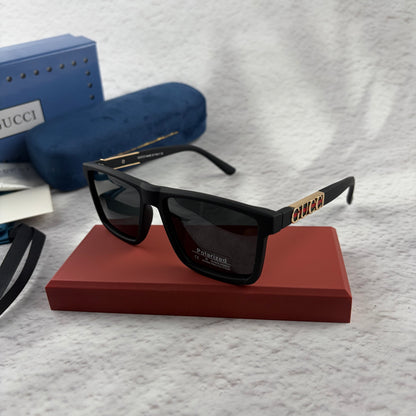 Matte black polarized sunglasses with gold logo detailing on temple arms, sitting on a red display b