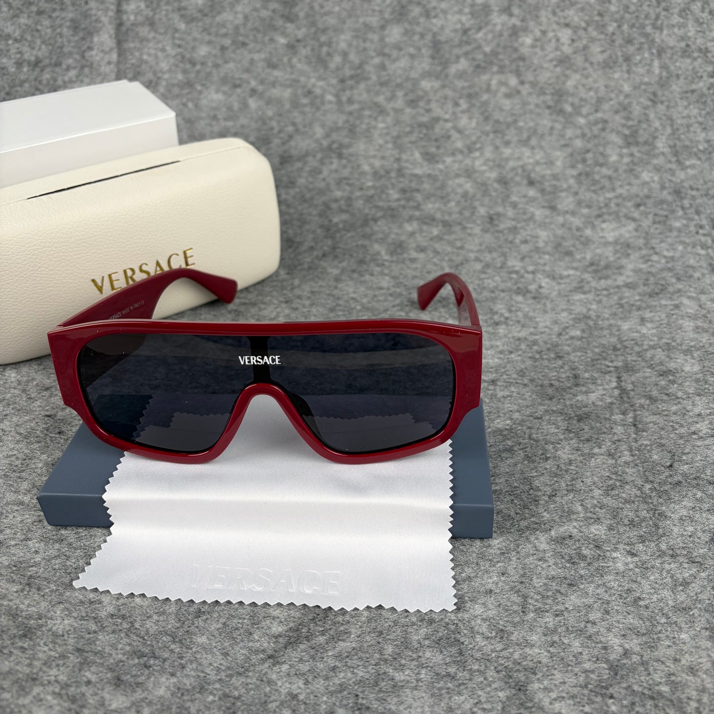 Oversized bold red shield sunglasses with dark lenses on a grey background with a white case.