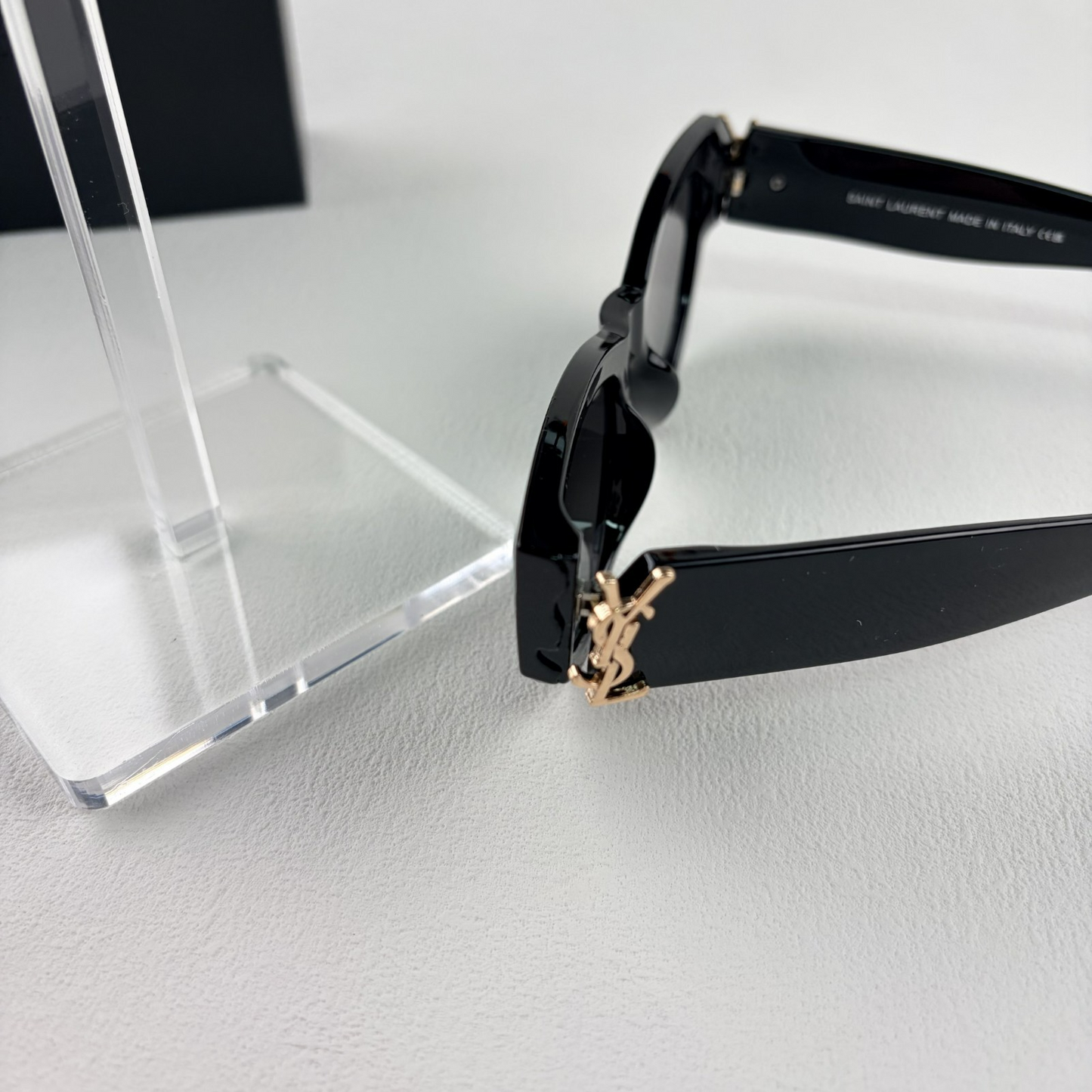 A pair of black cat-eye sunglasses with gold-tone hardware on the temples, displayed on a stand.