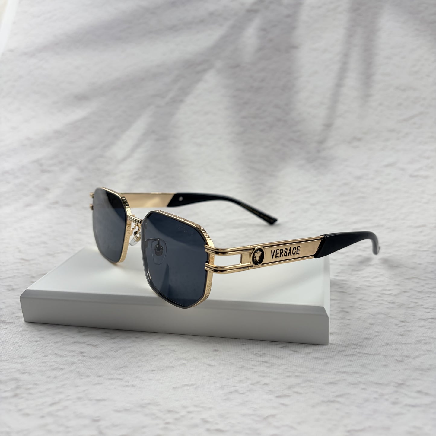 Gold tone metal frame geometric sunglasses with dark lenses on a white display block.