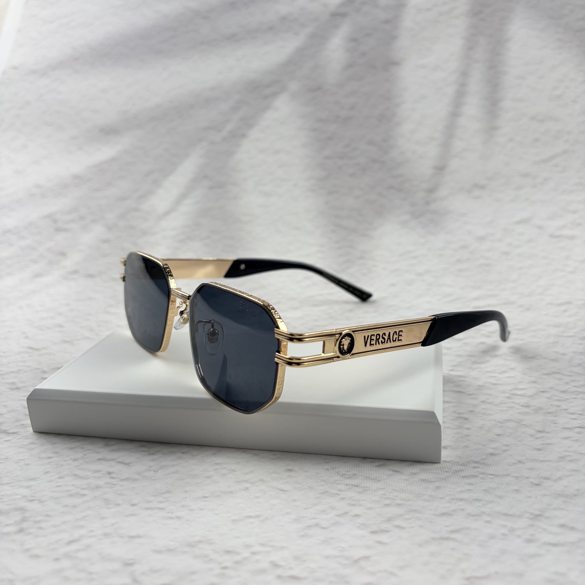 Gold tone metal frame geometric sunglasses with dark lenses on a white display block.