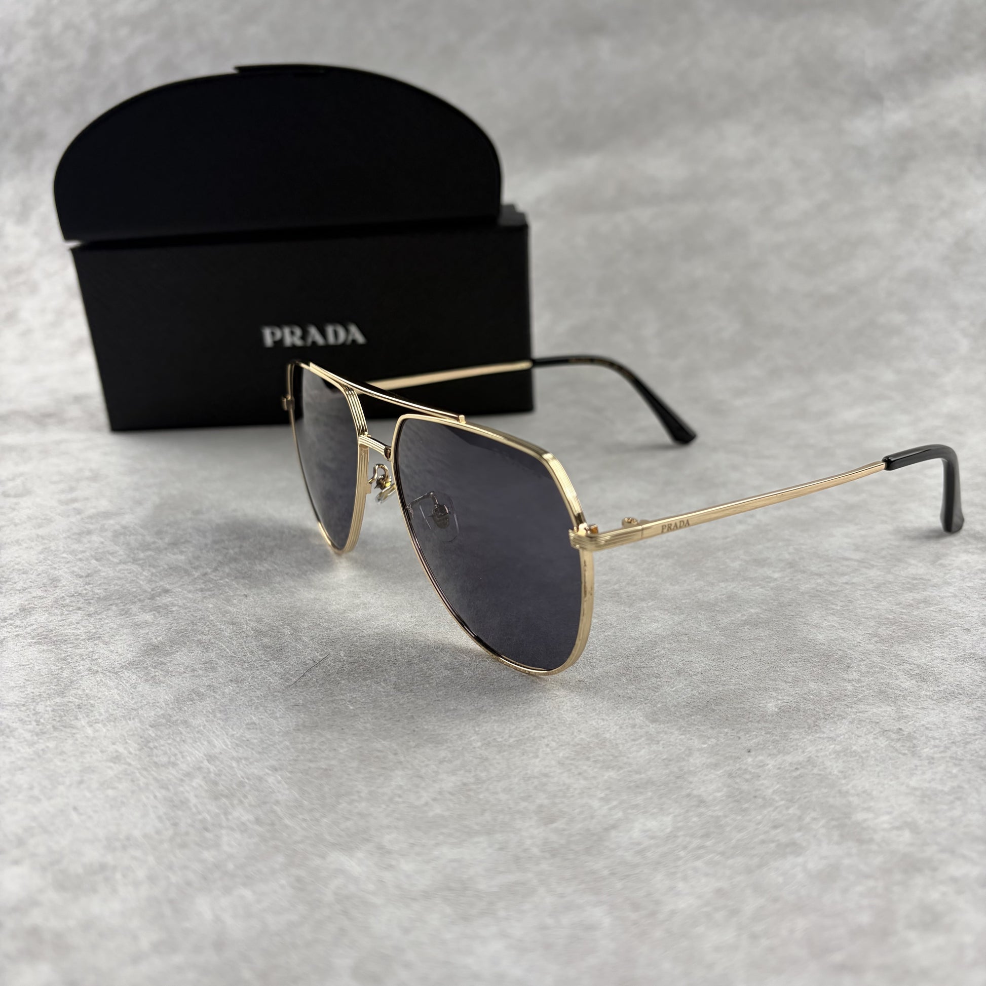 A pair of gold metal aviator sunglasses with dark lenses resting on a light grey textured background
