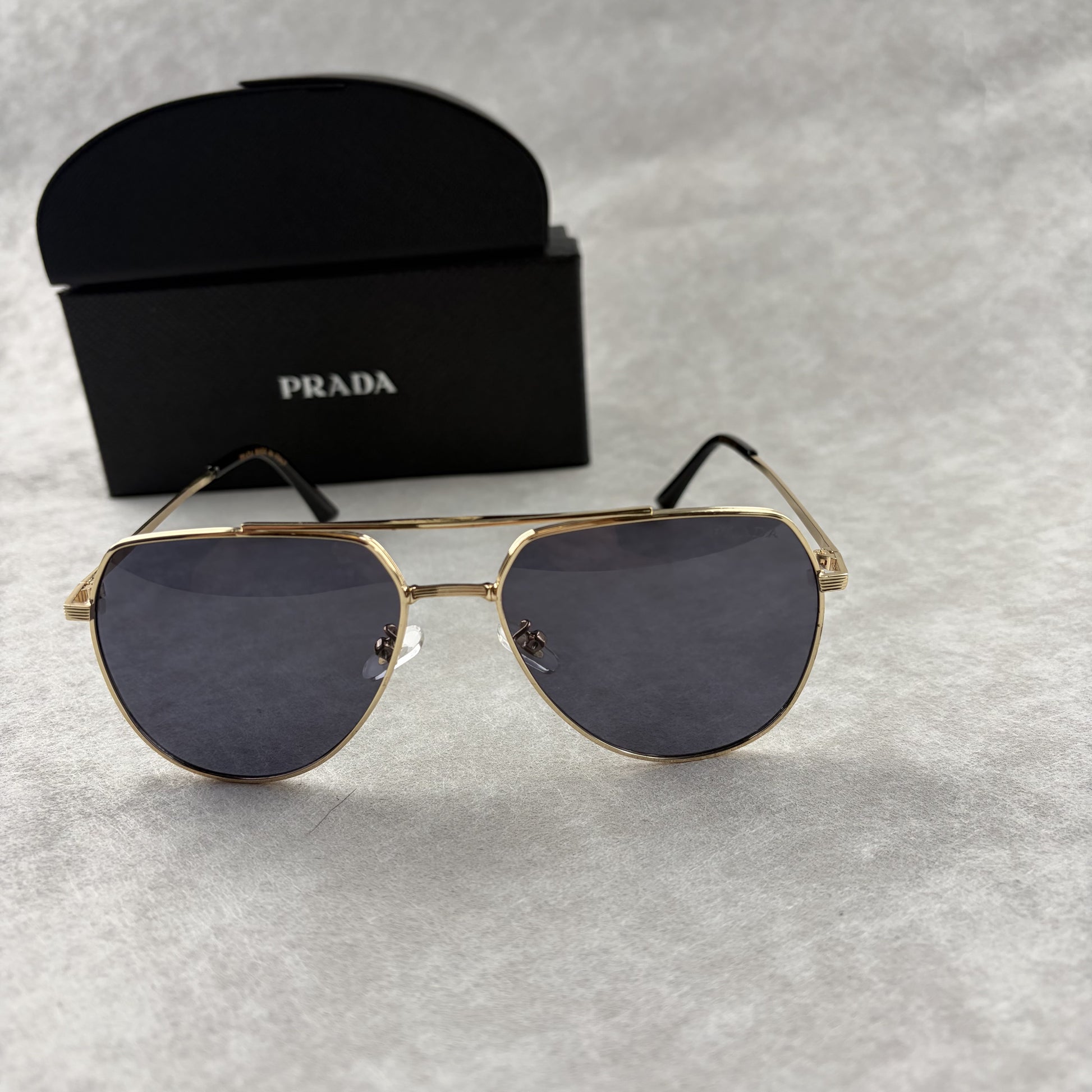 A pair of gold metal aviator sunglasses with dark lenses resting on a light grey textured background