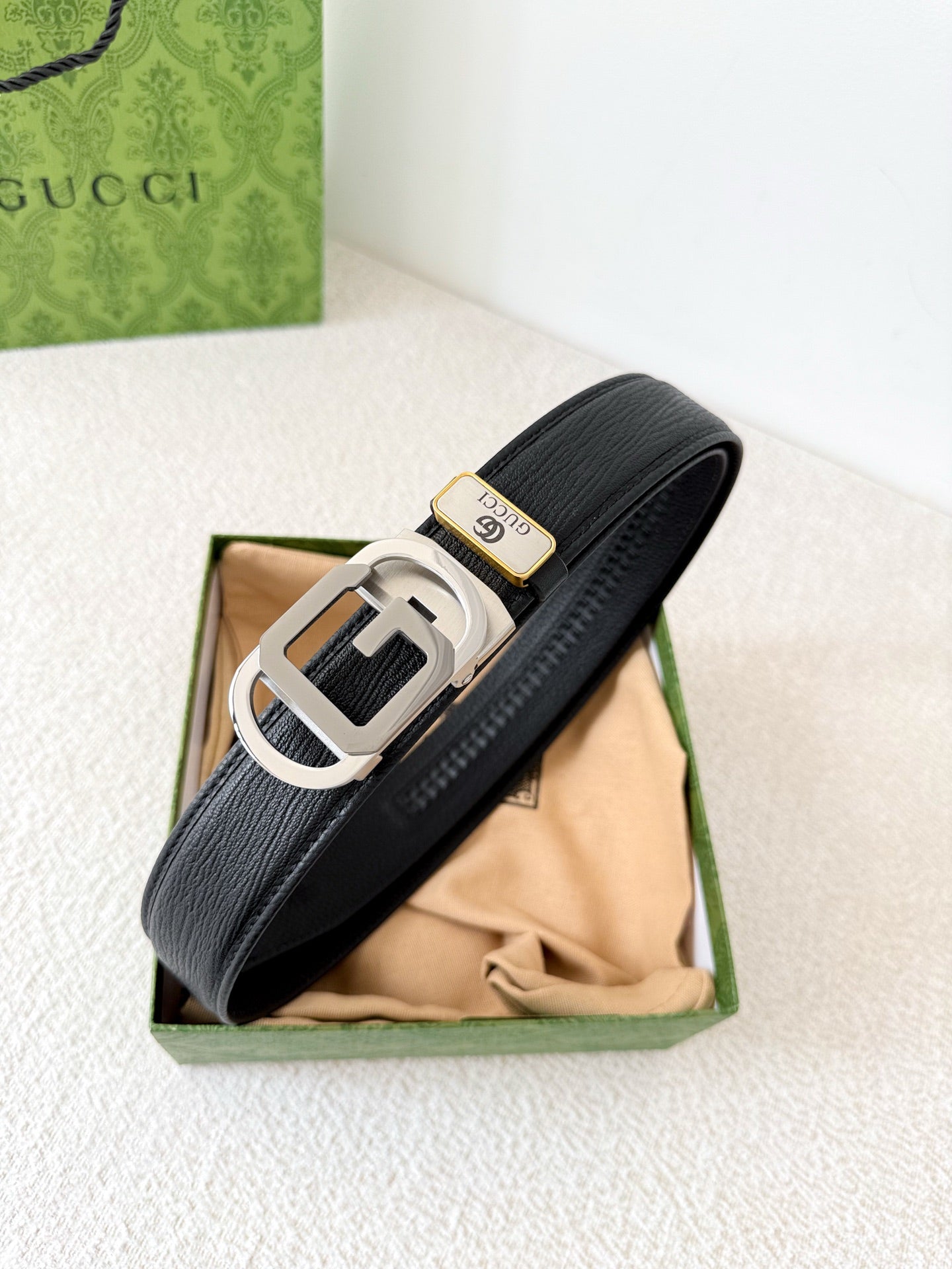 Black textured genuine leather belt with a modern metallic geometric buckle on a white surface.