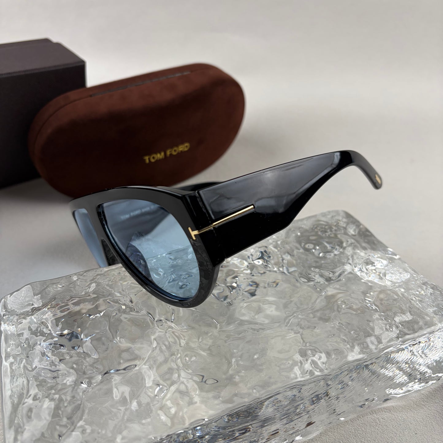 Black acetate oversized aviator sunglasses with blue tinted lenses resting on a clear ice-like block