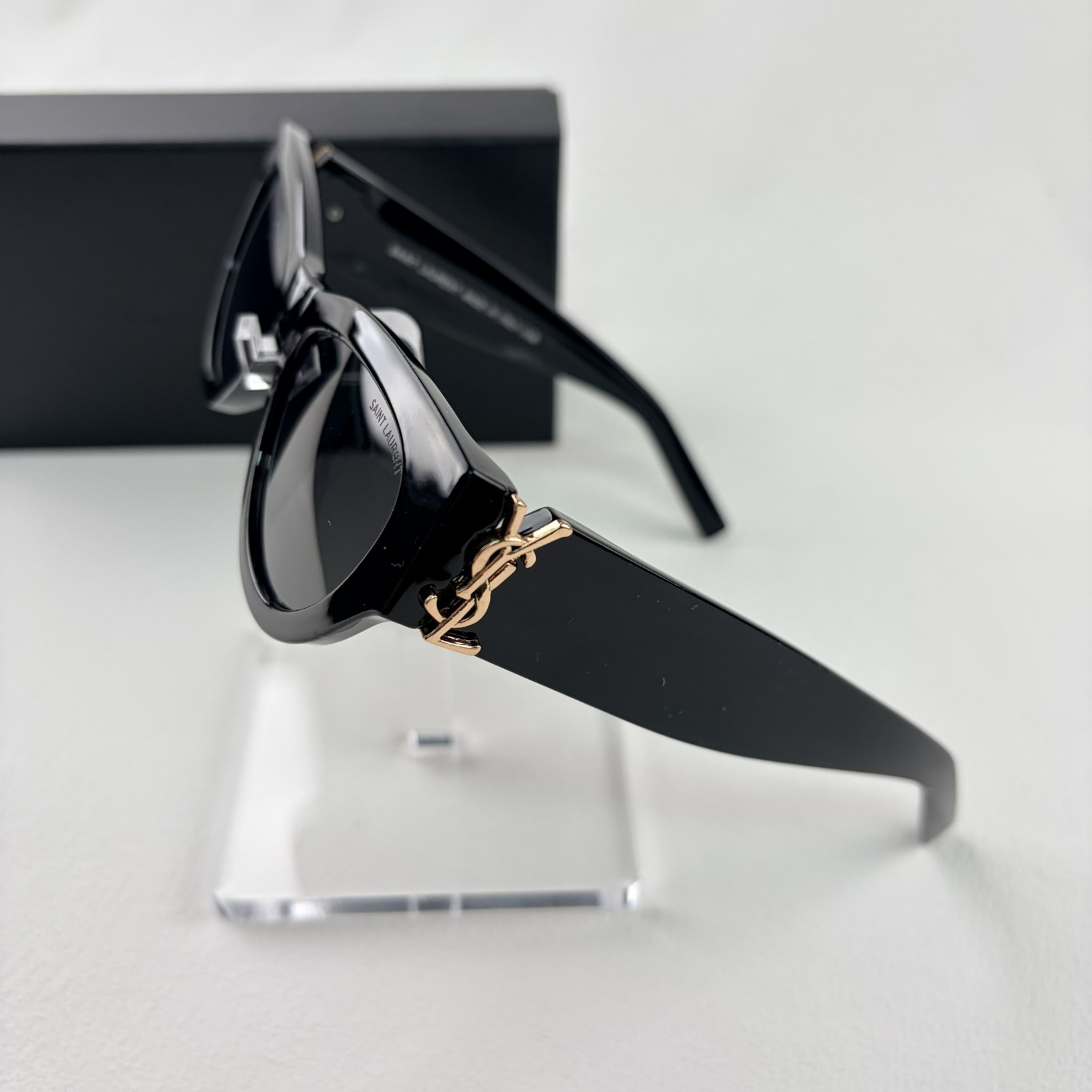 A pair of black cat-eye sunglasses with gold-tone hardware on the temples, displayed on a stand.