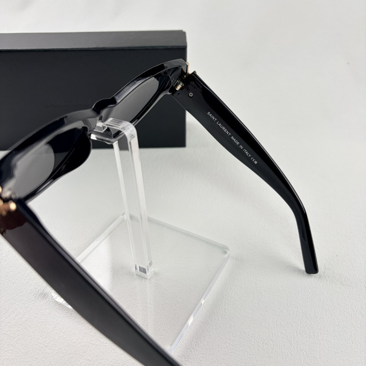 A pair of black cat-eye sunglasses with gold-tone hardware on the temples, displayed on a stand.