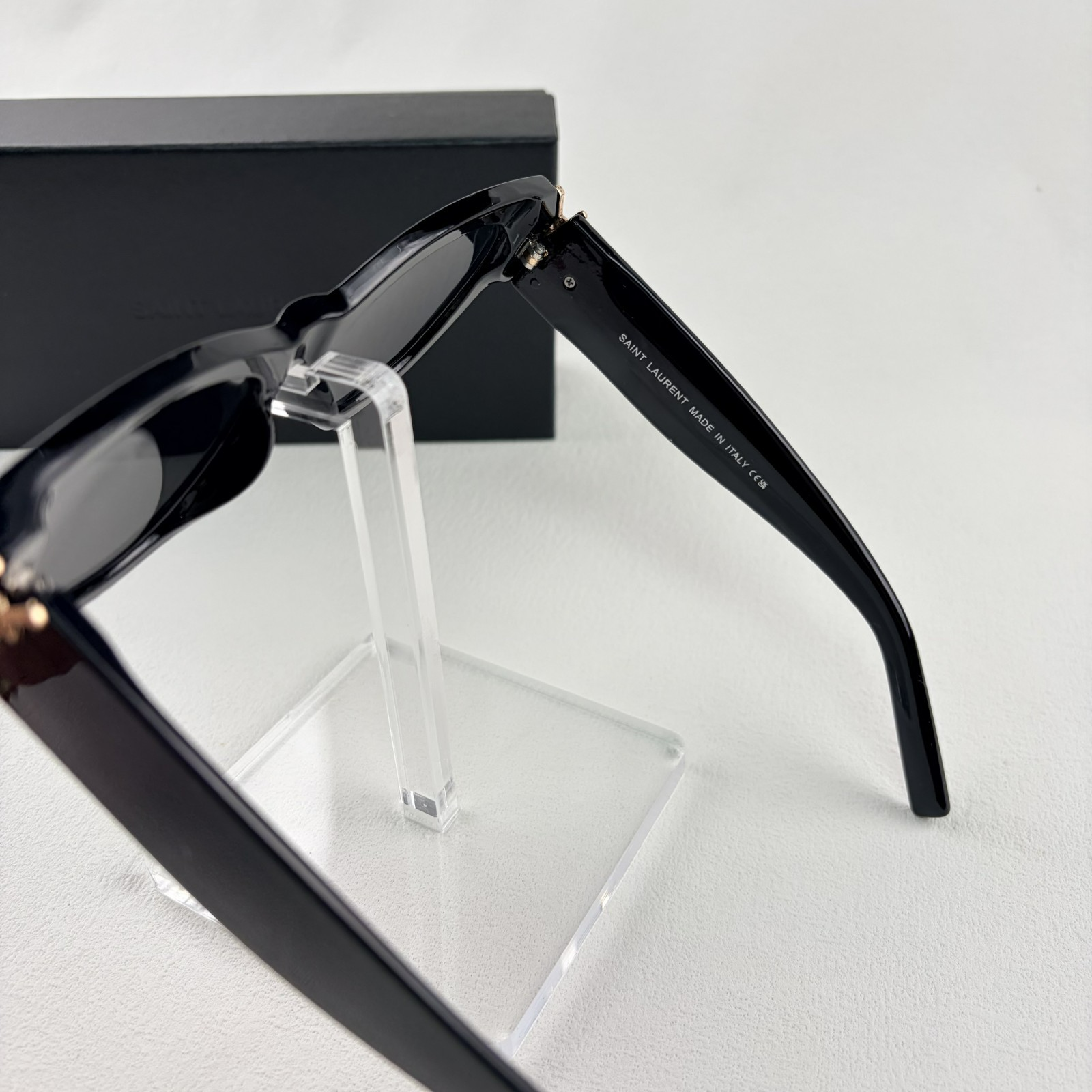 A pair of black cat-eye sunglasses with gold-tone hardware on the temples, displayed on a stand.
