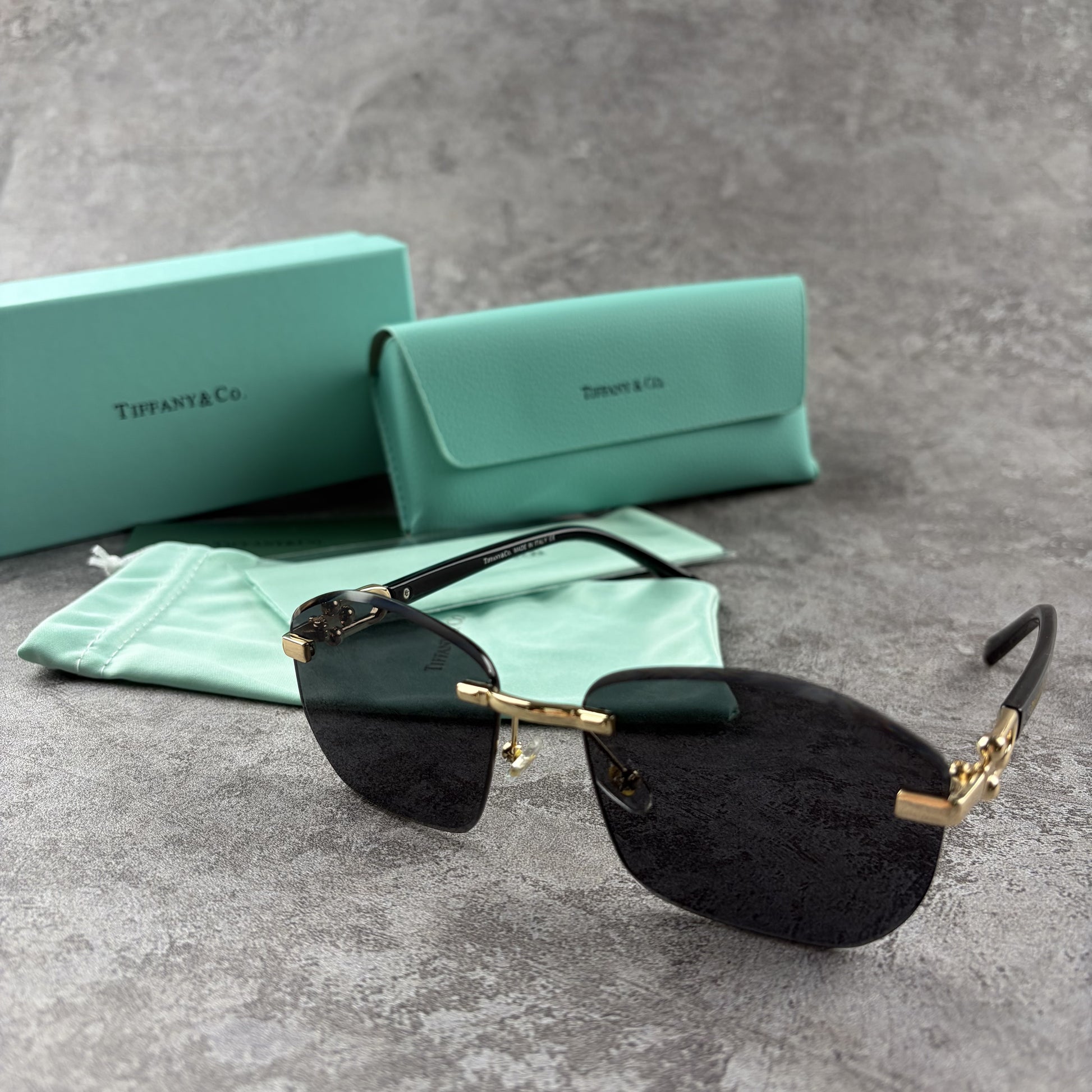 Rimless gradient sunglasses with gold-tone metal frames and black temple arms on a grey surface.