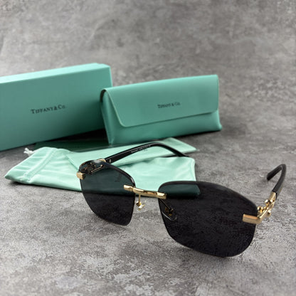 Rimless gradient sunglasses with gold-tone metal frames and black temple arms on a grey surface.