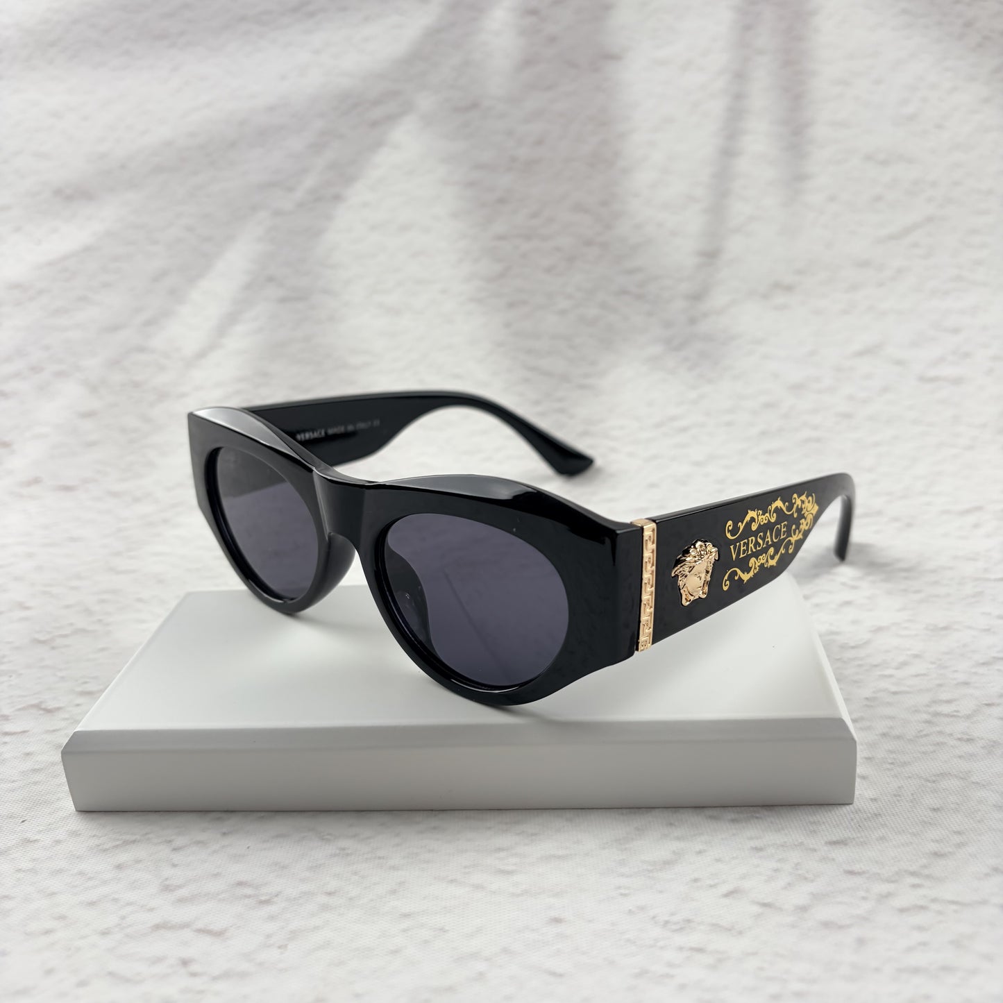 Black cat-eye sunglasses featuring gold-toned baroque temple embellishments on a white textured base