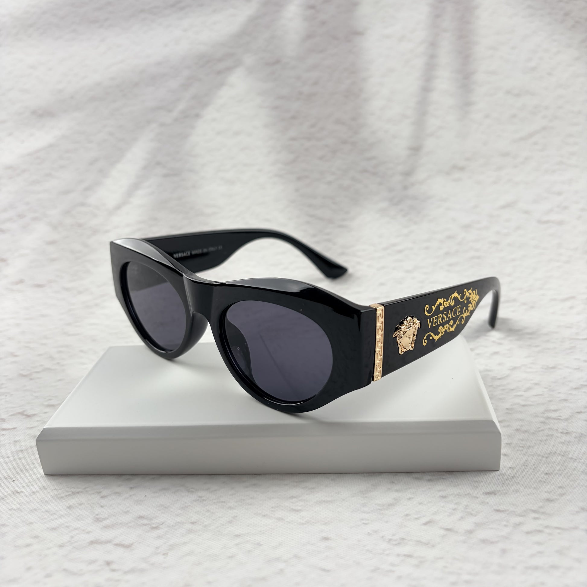 Black cat-eye sunglasses featuring gold-toned baroque temple embellishments on a white textured base