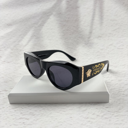 Black cat-eye sunglasses featuring gold-toned baroque temple embellishments on a white textured base