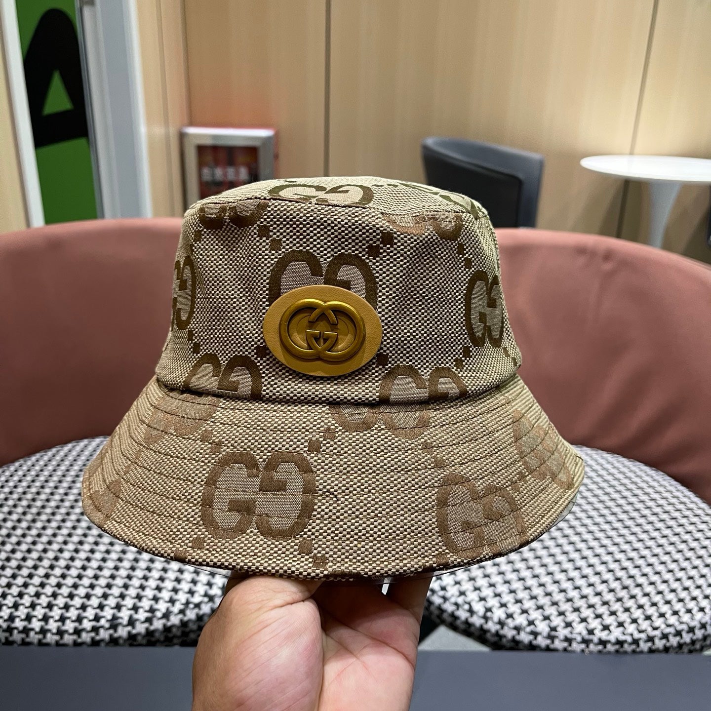 A beige canvas bucket hat with an all-over brown monogram pattern and a decorative gold-toned emblem