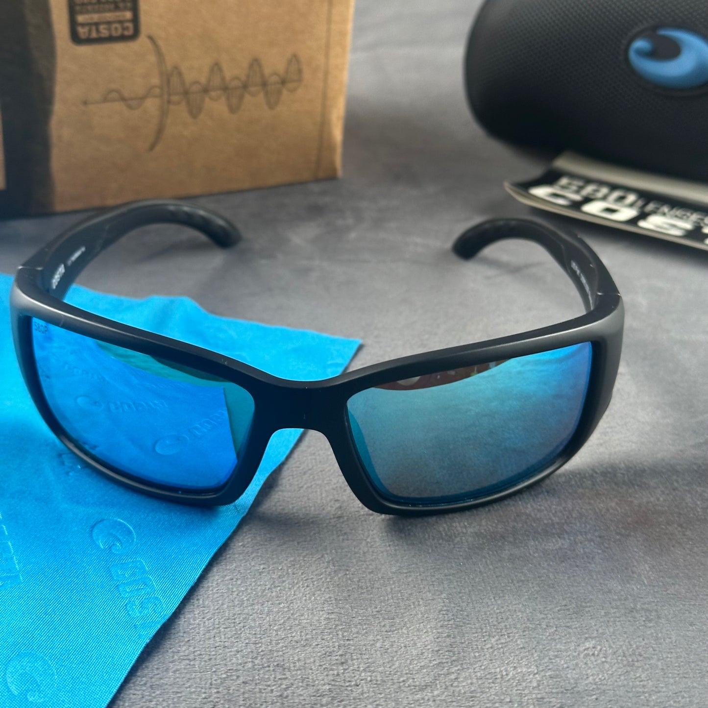 Matte black frame sport sunglasses with blue mirror lenses, including a protective case and cloth.