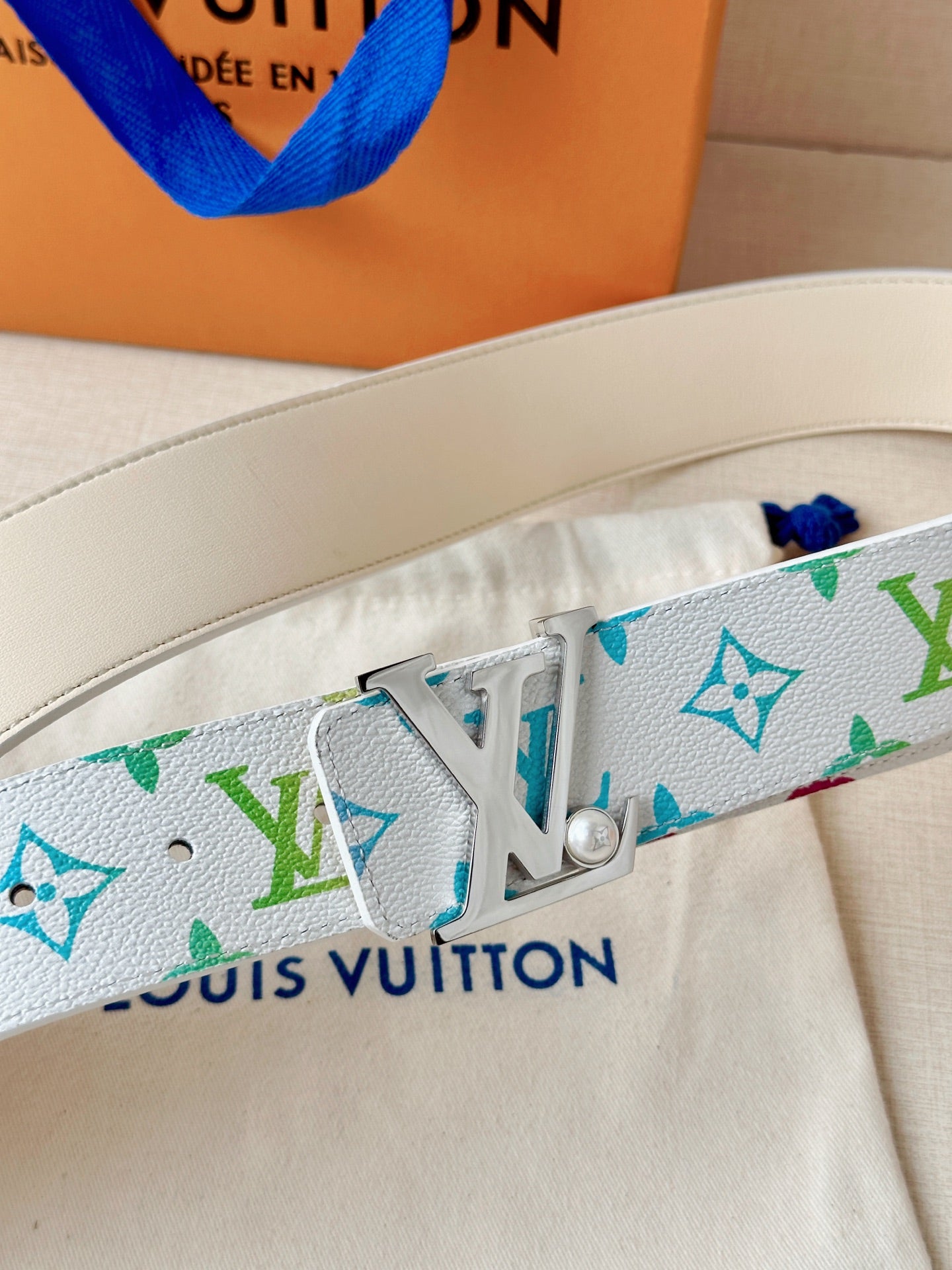 A white leather belt with colorful monogram print and a silver buckle with a pearl accent.