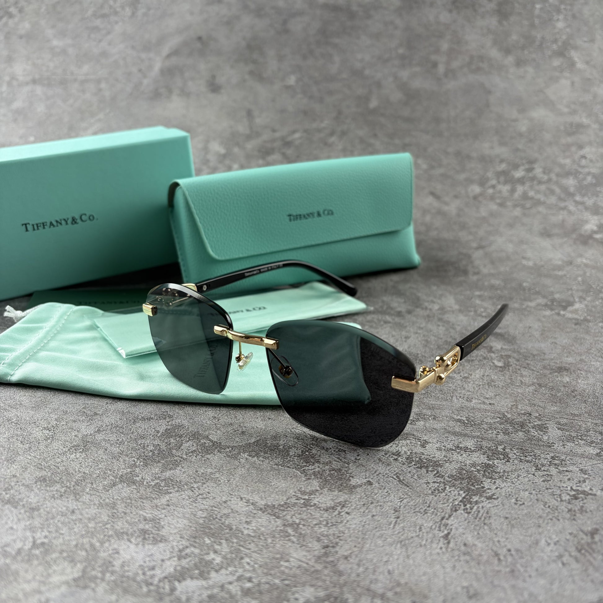 Rimless gradient sunglasses with gold-tone metal frames and black temple arms on a grey surface.
