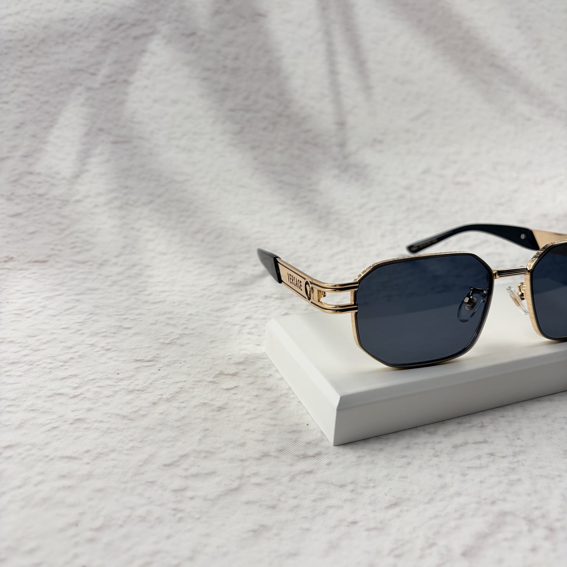 Gold tone metal frame geometric sunglasses with dark lenses on a white display block.