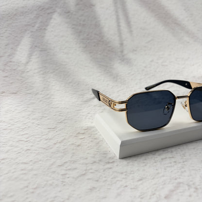 Gold tone metal frame geometric sunglasses with dark lenses on a white display block.