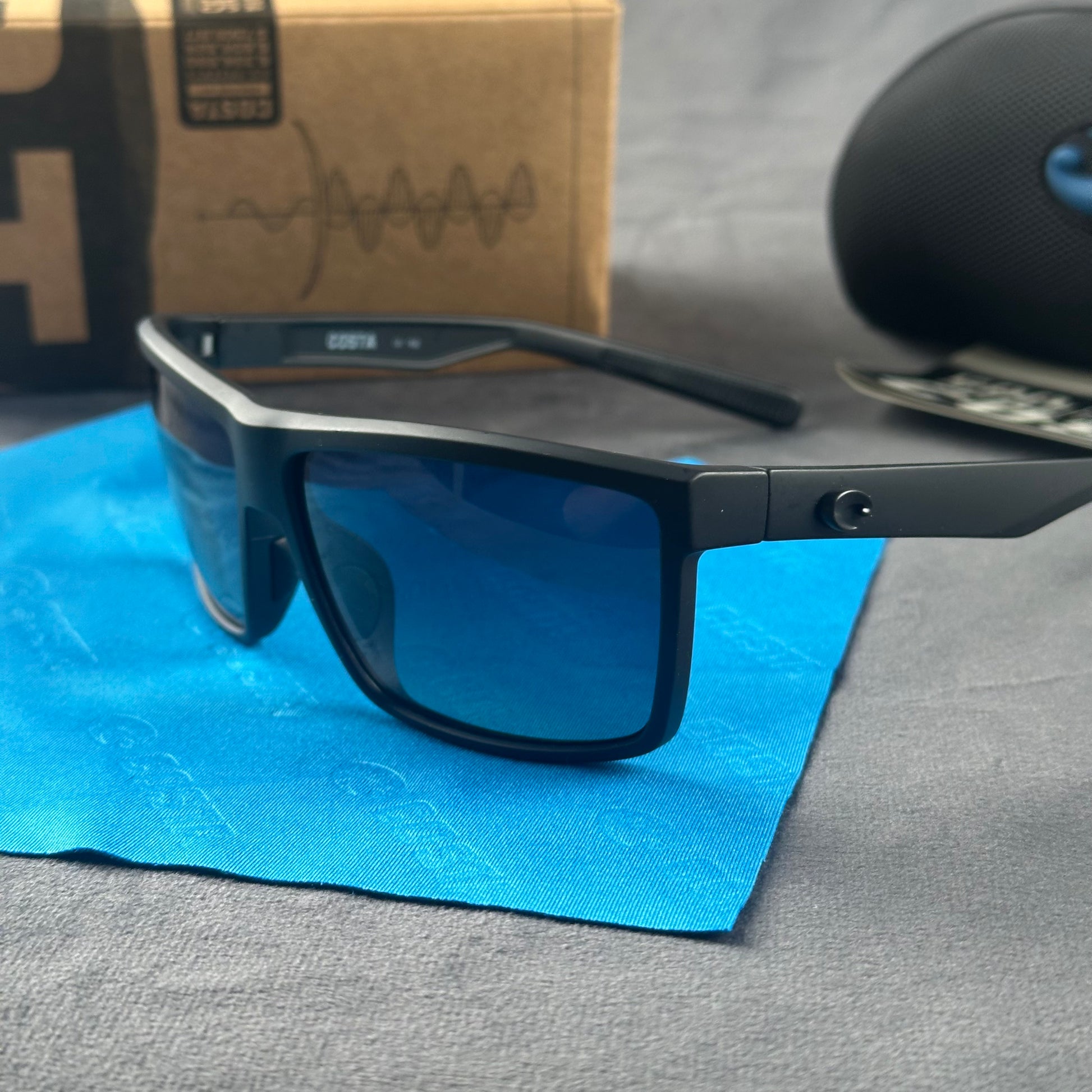 Matte black sport sunglasses with polarized blue-tinted lenses, hard case, and cleaning cloth.