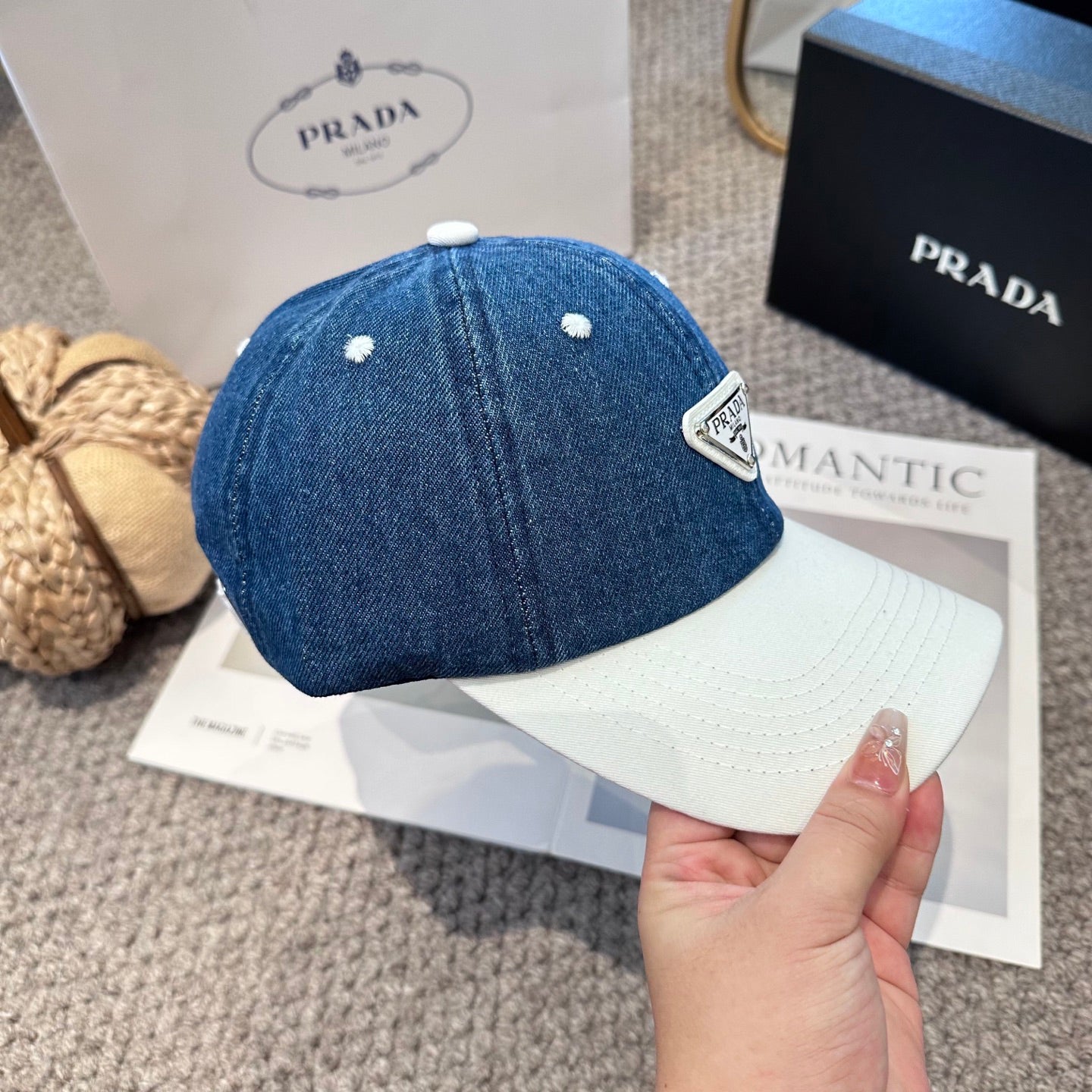 A stylish blue denim baseball cap with a white brim and a triangular metal-look logo patch.