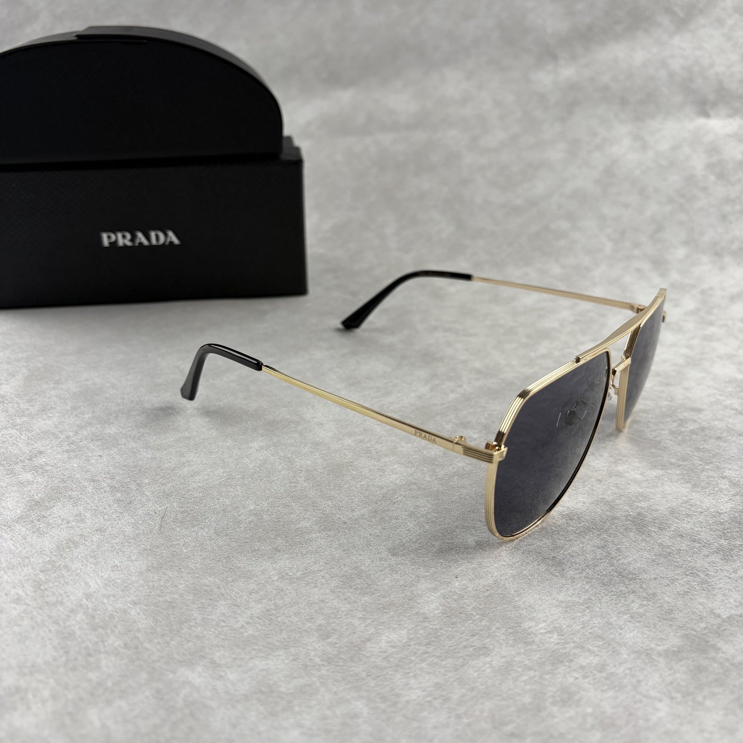 A pair of gold metal aviator sunglasses with dark lenses resting on a light grey textured background