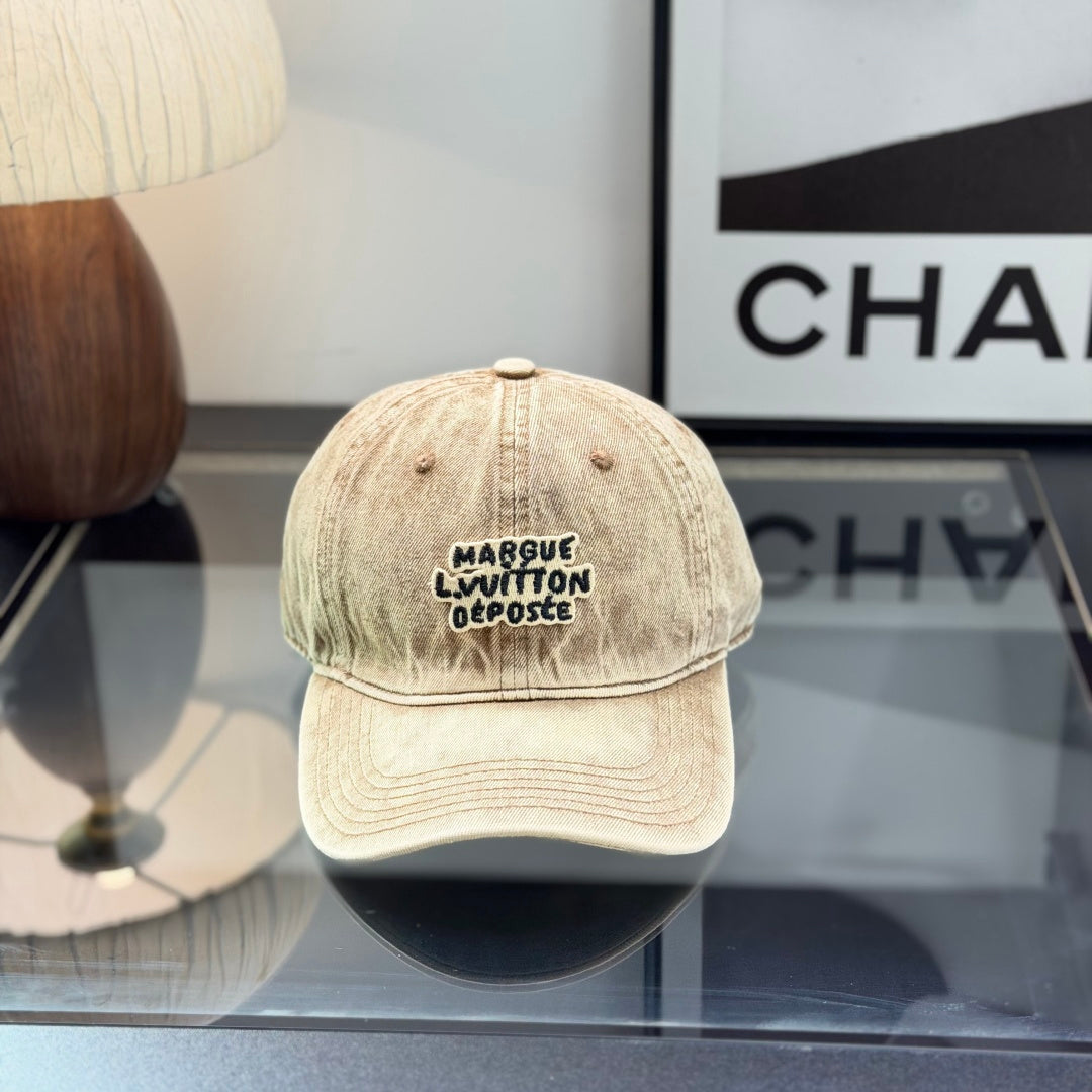 Vintage style distressed light brown denim baseball cap with embroidered letter patch on front.